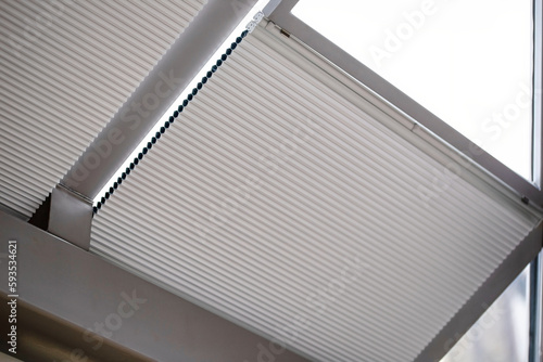 Motorized pleated blinds on the roof windows. Cellular pleated blinds for skylights, beige color. Honeycomb curtains on glass roof. Selective focus. photo