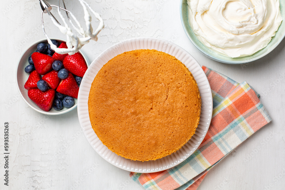 Cooking and baking vanilla sponge cake with berries, strawberries and blueberries, and whipped cream. Homemade culinary, summer fruit dessert. Top view of ingredient, white background.