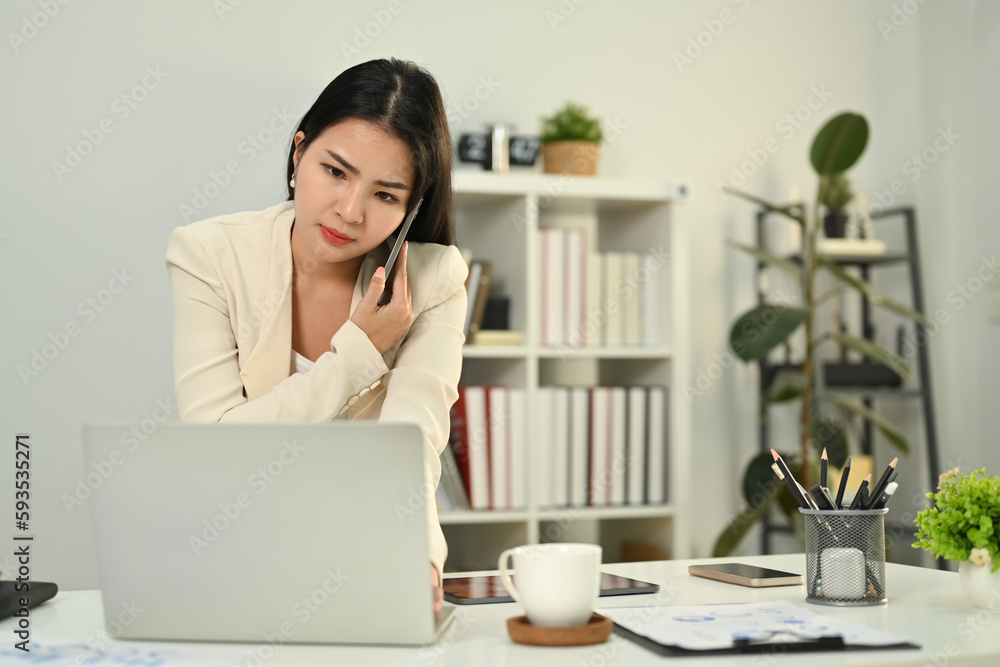 Serious female investment advisor having unpleasant phone conversation, consulting client at working desk Serious female investment advisor having unpleasant phone conversation, consulting client at working desk