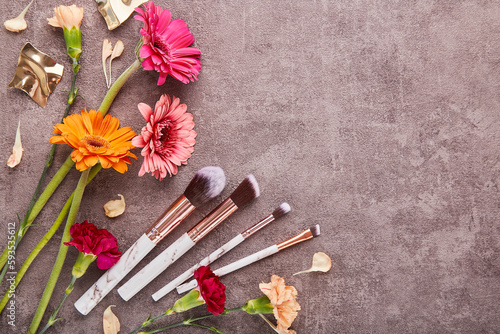Aesthetic make up brushes set among arrangement of gerbers, asters flowers with copy space. Makeup artist professional tools © Natalia