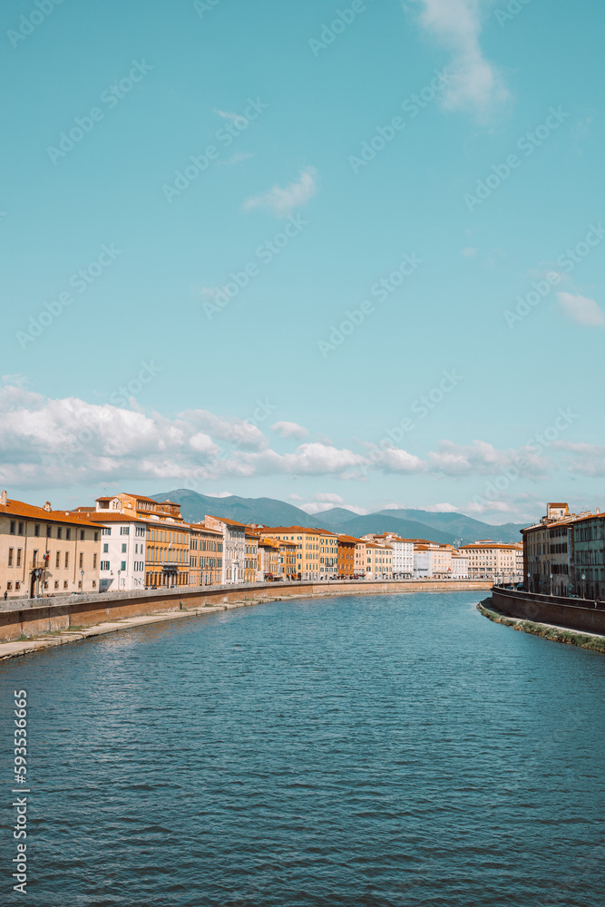 A beautiful view of buildings along the Arno river in Pisa, Italy. A bridge passes over the river and houses on both sides are overlooking the water