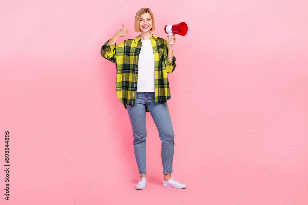 Full size photo of pretty young girl show thumb up megaphone dressed stylish checkered yellow look isolated on pink color background Full size photo of pretty young girl show thumb up megaphone dressed stylish checkered yellow look isolated on pink color background