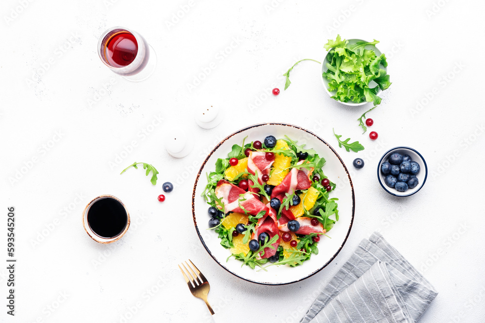 Gourmet salad with smoked duck fillet, fruit and berries, arugula and lettuce, white table background, top view