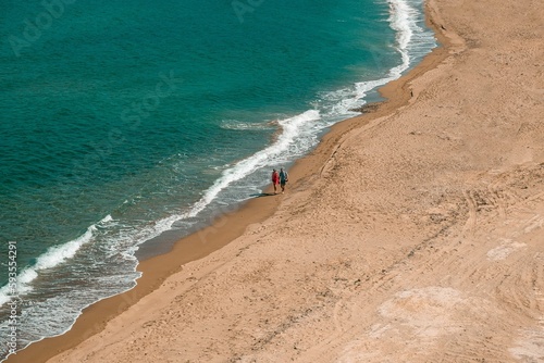 Aerial shot of a couple walking along a beach against the blue sea on a summer day