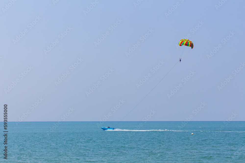 blue motorboat on horizon in Andaman Sea rolls man under parachute, shallow DOF,copy space. blue motorboat on horizon in Andaman Sea rolls man under parachute, shallow DOF,copy space.