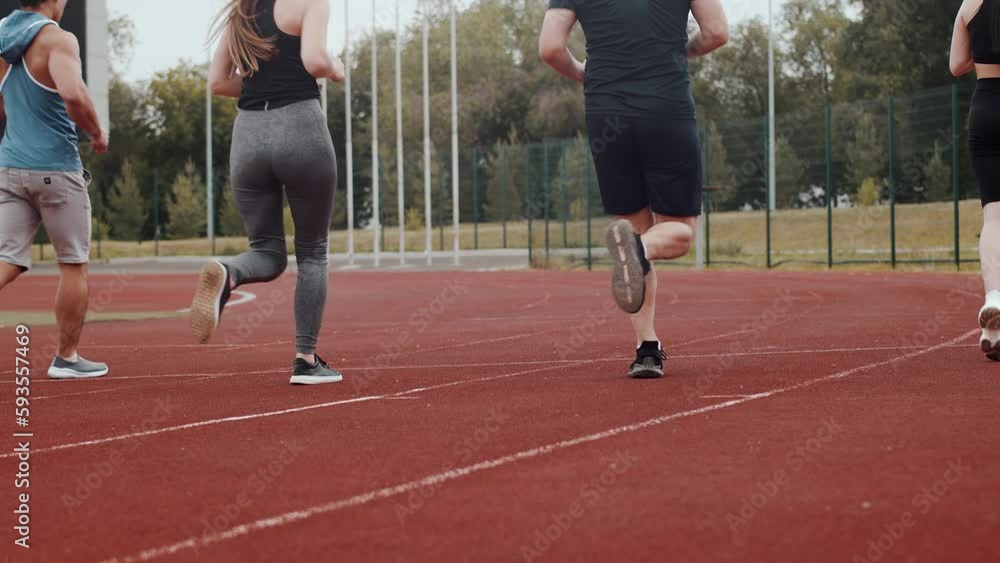 Group of athletes in sportswear calmly runs next to each other on the running track of an outdoor stadium in the rear view. Sportsmen enjoy joint training Group of athletes in sportswear calmly runs next to each other on the running track of an outdoor stadium in the rear view. Sportsmen enjoy joint training