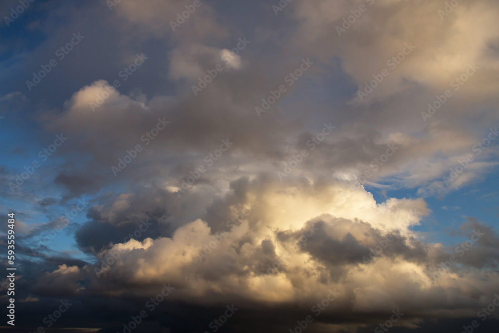 Storm cloudy epic dramatic sky with dark rain grey cumulus cloud in yellow sunlight and blue sky background texture, thunderstorm, heaven