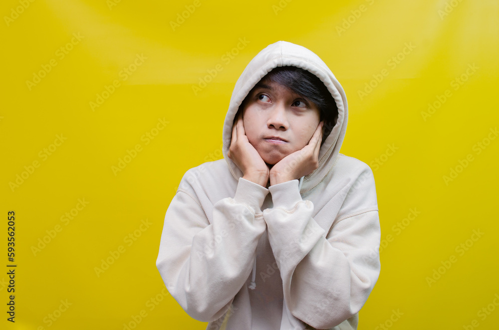 A thoughtful, confused Asian man thinking and wondering whether to choose something isolated on a yellow white background. Stylish asian man is thinking and wondering. A thoughtful, confused Asian man thinking and wondering whether to choose something isolated on a yellow white background. Stylish asian man is thinking and wondering.