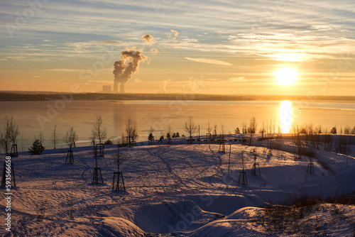 the shore of the st  rmthal lake in winter. the meadows are covered with snow and the lake has a layer of ice. the setting sun colors everything orange.