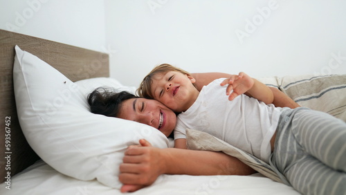 Mother and child laying in bed smiling. Happiness motherhood lifestyle concept. Little boy hugs mom cheek to cheek