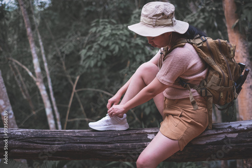 Asian woman tying shoelaces to backpack hiking in deep forest