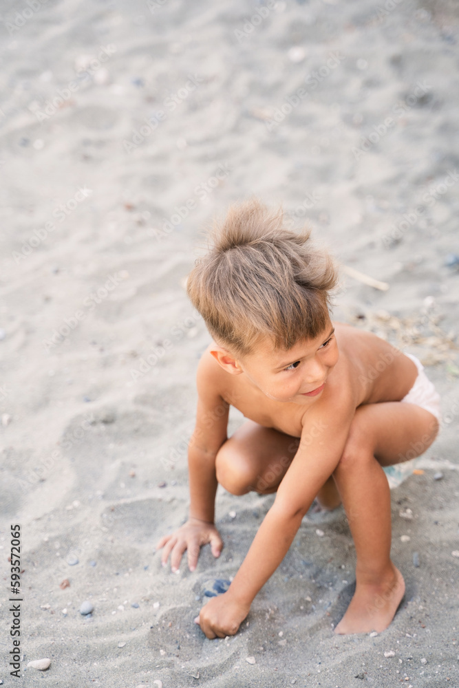 Little boy wearing diaper is playing on sandy beach during summer vacation Little boy wearing diaper is playing on sandy beach during summer vacation