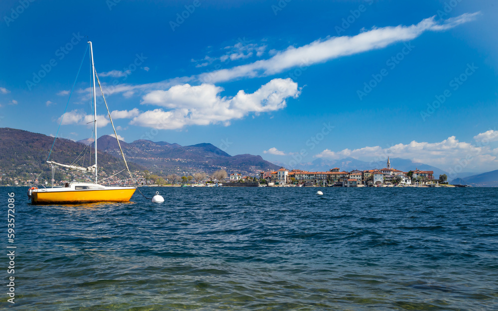 yellow sailing boat front of the borromean island isola superiore in the italian lake lago maggiore on blue sunny sky background. italy vacation travel and tourism concept