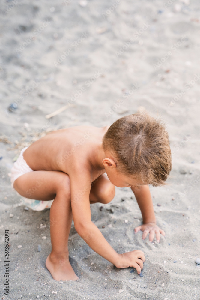 Little boy wearing diaper is playing on sandy beach during summer vacation Little boy wearing diaper is playing on sandy beach during summer vacation