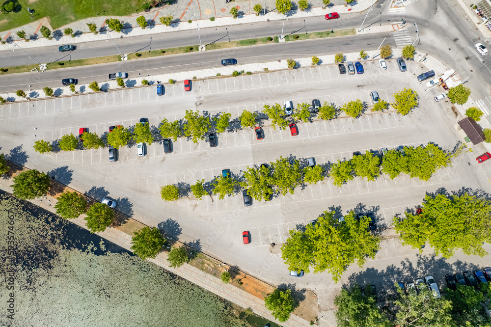 Public city parking for cars among the trees in the park near lake. Aerial view. Drone, top view Public city parking for cars among the trees in the park near lake. Aerial view. Drone, top view