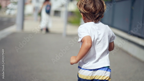 One joyful small boy running outdoors in city street sidewalk. Back of child runner in urban environment