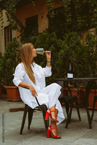 young fashionable woman drinking white wine at a table in a beautiful street cafe