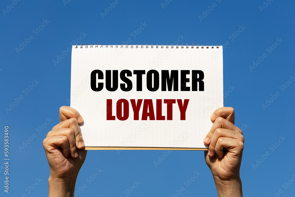 Customer loyalty text on notebook paper held by 2 hands with isolated blue sky background. This message can be used as business concept about customer loyalty. Customer loyalty text on notebook paper held by 2 hands with isolated blue sky background. This message can be used as business concept about customer loyalty.