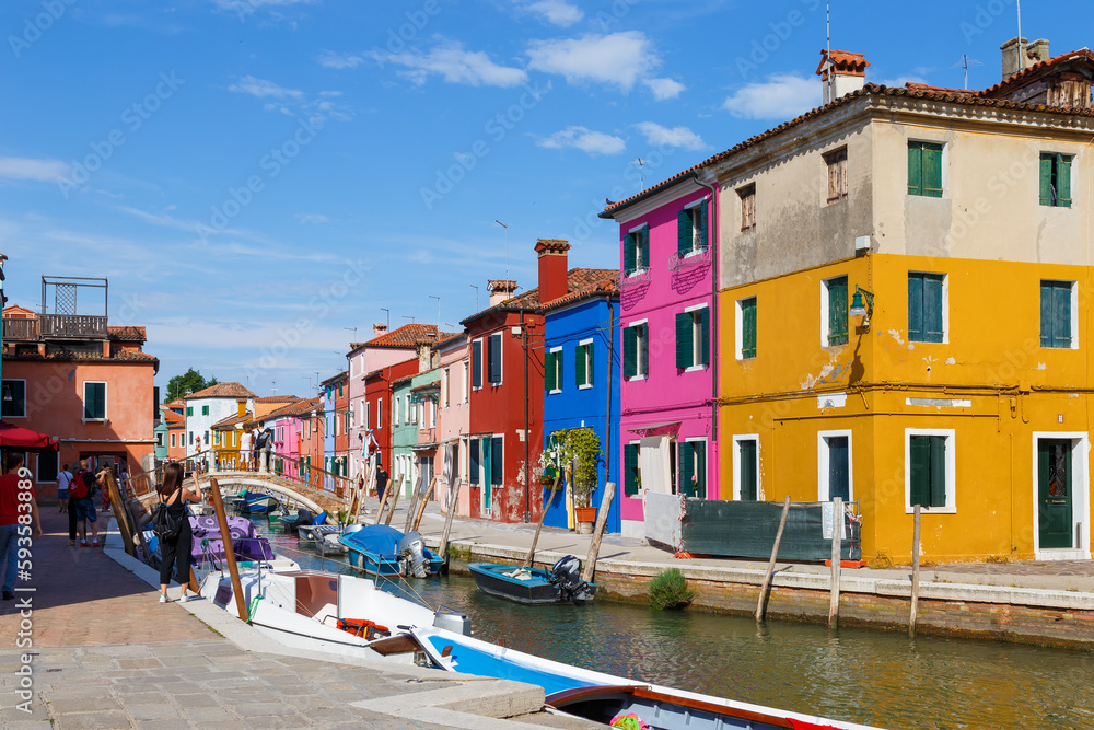 Multicolored colorful houses in Venice on the island of Burano. Narrow canal with motor boats along the houses. Summer sunny day. Selective focus.