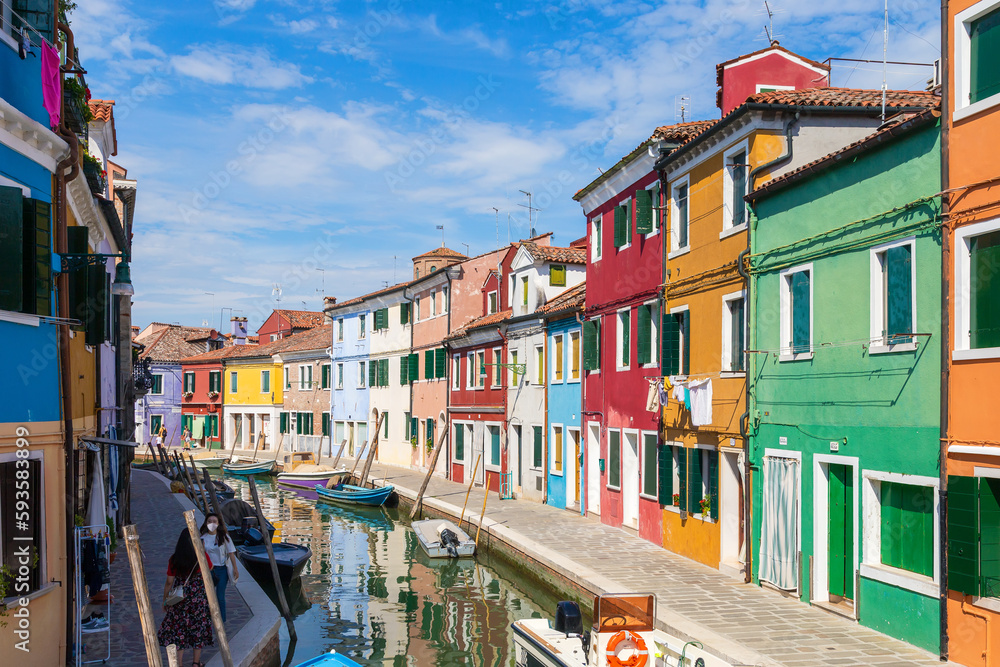 Multicolored colorful houses in Venice on the island of Burano. Narrow canal with motor boats along the houses. Summer sunny day. Selective focus.