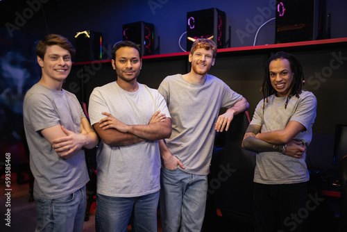 Cheerful interracial team crossing arms and looking at camera in gaming club.