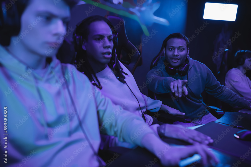 Excited indian man pointing with finger near interracial friends in computer club.