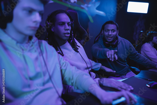 Excited indian man pointing with finger near interracial friends in computer club. © LIGHTFIELD STUDIOS