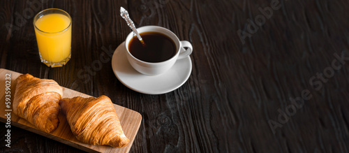 Two croissants on a wooden cutting board. Rustic dark table. Food banner. Tasty fresh croissant, jam, orange juice. Continental breakfast served with freshly baked pastry. Close up view, Good morning