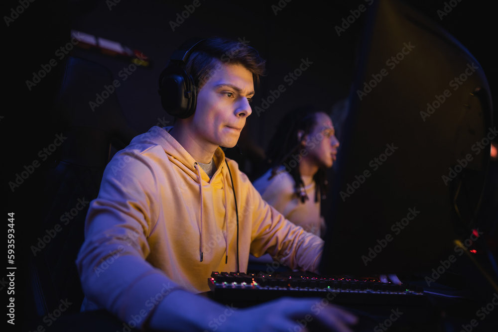 Young man in headphones playing computer game in cyber club with lighting. Young man in headphones playing computer game in cyber club with lighting.