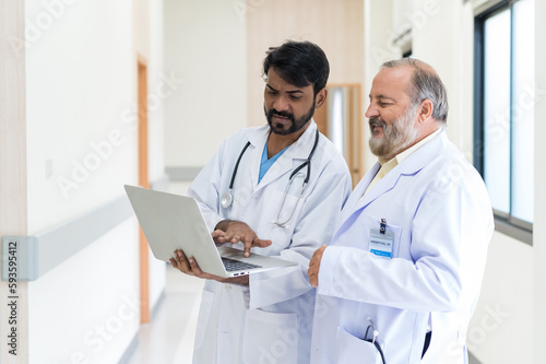 Concentrated mature and young male doctors in white medical uniforms look at laptop computer and discuss patient anamnesis together. team brainstorming make decision concept.