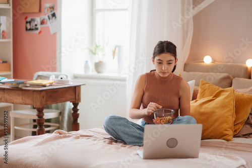 Young teenage girl looking at her latop and eating something. photo