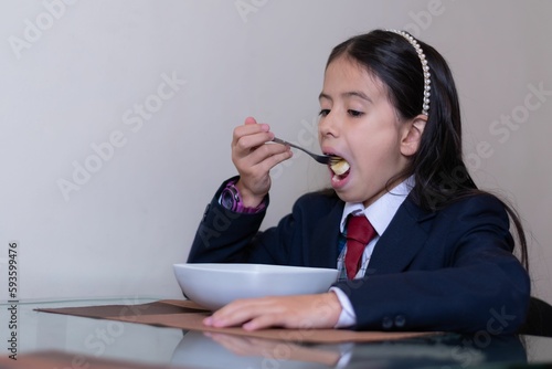 Hispanic little girl wearing a school uniform eating food from a bowl