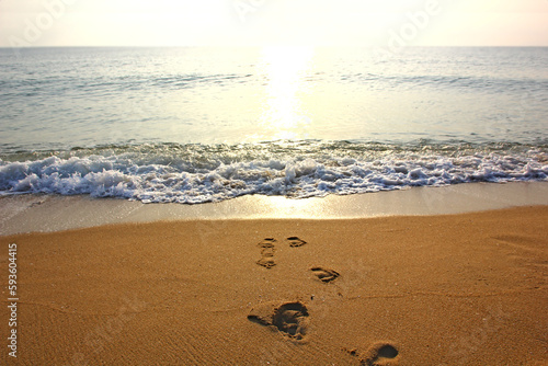 Footprints on the sand at the beach against the backdrop of the rising sun on the sea.
