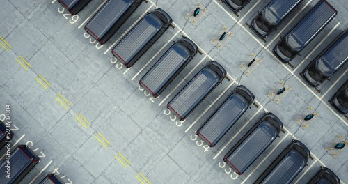 Drone overhead shot, huge fleet of electric EV delivery vans are being charged in company parking garage