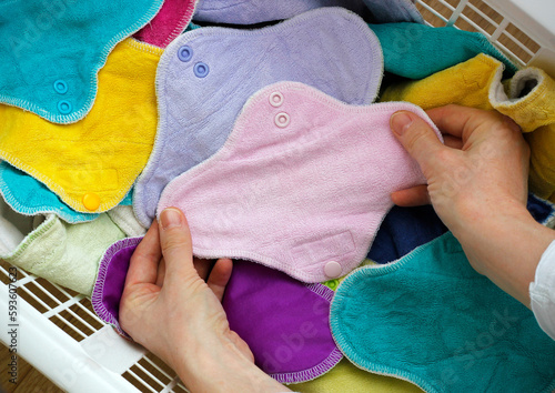 Female hands holding a pink cloth pad inside a laundry basket full of colorful cloth bamboo washable sanitary napkins. Eco-friendly reusable fabric pads, zero waste alternatives. Women hygiene concept