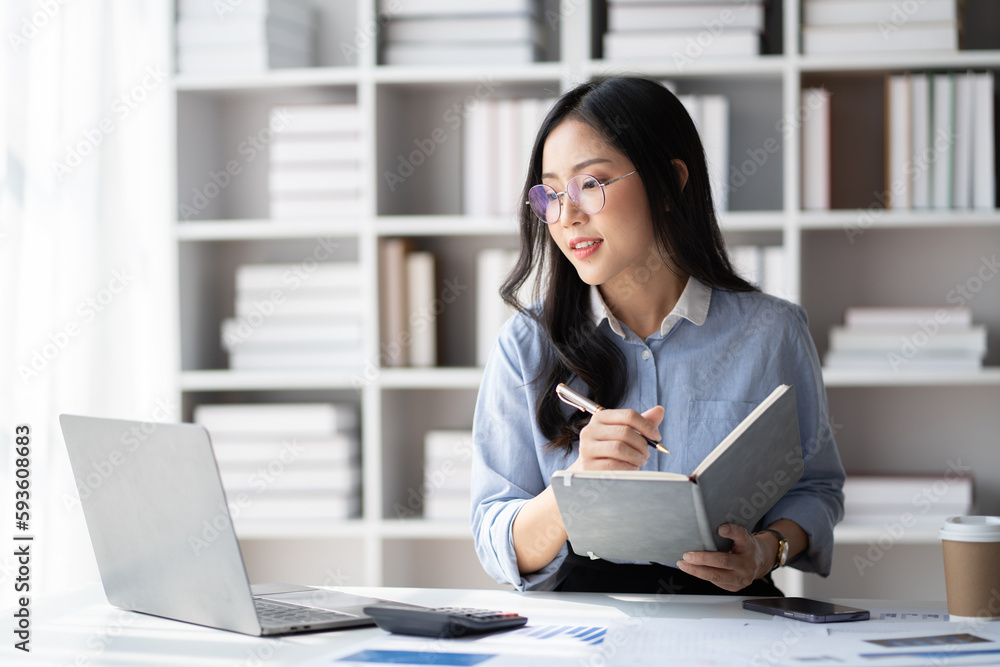 Young smart Asian businesswoman with glasses writing her idea while working in her office room. Young smart Asian businesswoman with glasses writing her idea while working in her office room.