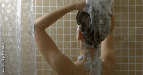 Young woman washing her hair in the shower with shampoo