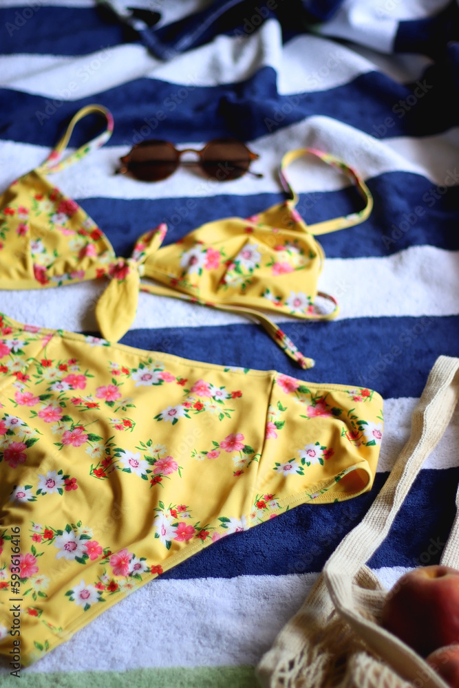 Striped beach towel, floral yellow swimsuit, sunglasses and mesh bag with peaches. Cute beach essentials. Selective focus.