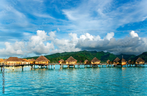 Fototapeta Naklejka Na Ścianę i Meble -  Overwater bungalows stretching out across the lagoon and a few catamarans in a quiet bay in Bora Bora island, Tahiti. Romantic honeymoon destination.