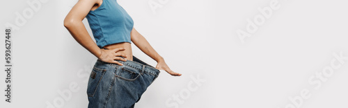 Young pretty asian chinese woman weight loss with oversize big blue jean pants, isolated background.