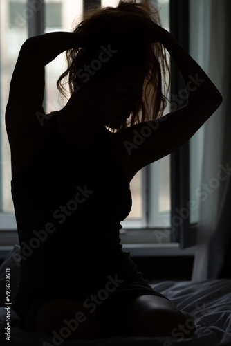 Silhouette of a beautiful slender woman sitting on a bed