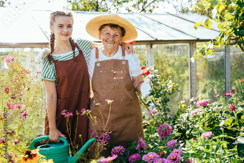 Teenager grandchild helping to her elderly grandmother at the greenhouse in summer outside. Granddaughter and her pensioner senior granny working together at countryside. photo