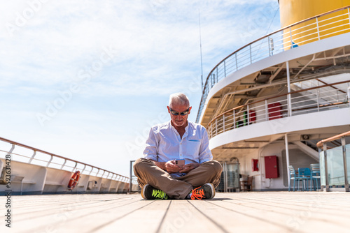 happy handsome middle aged man using smartphone on the deck of a cruise ship