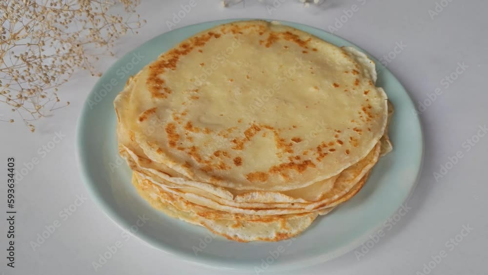 A plate of pancakes for breakfast. Fresh, homemade pancakes. Women's hands roll a thin pancake into a tube A plate of pancakes for breakfast. Fresh, homemade pancakes. Women's hands roll a thin pancake into a tube