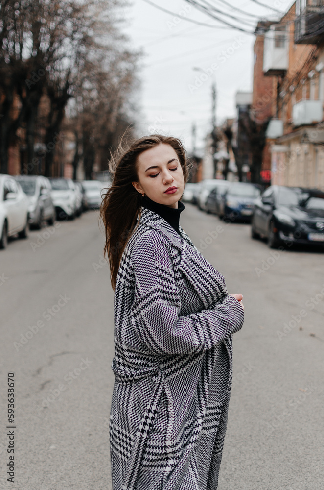 Fototapeta premium The girl is standing on the street in a gray coat