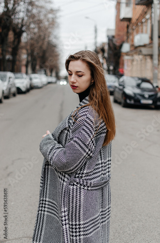 The girl is standing on the street in a gray coat