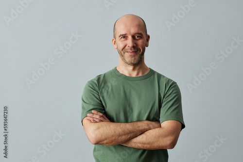 Minimal waist up portrait of mature bald man smiling at camera while standing confidently with arms crossed, copy space