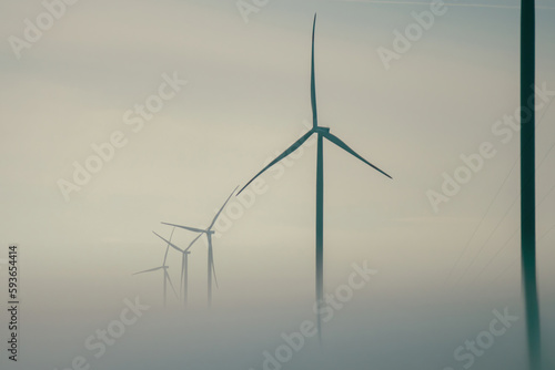 Windmills tops with rotor blades producing alternative form of energy for stations. Wind turbines covered with dense fog against grey sky © SlavaStock