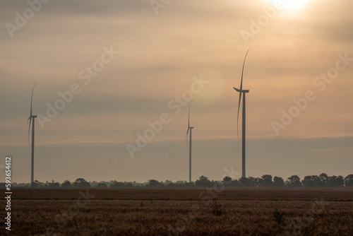Sunset illuminates windfarm with turbines generating green energy. Windmills with rotor blades producing alternative energy source