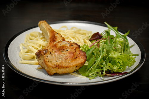 Fried veal rib steak with fresh salad and linguine pasta, steak in a frying pan